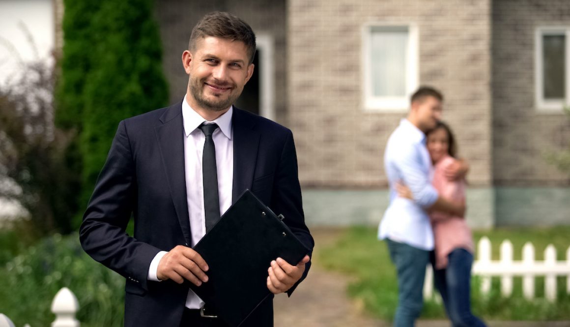 Smiling broker standing with documents, happy family hugging near their new home