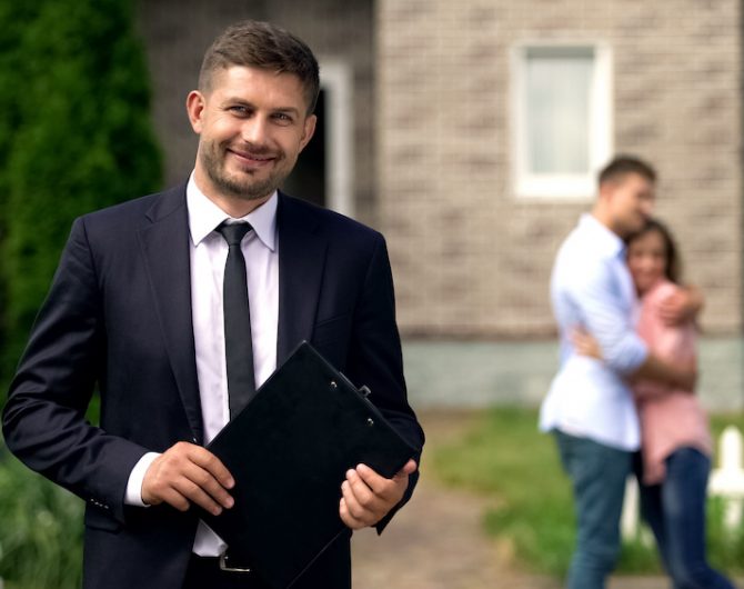 Smiling broker standing with documents, happy family hugging near their new home